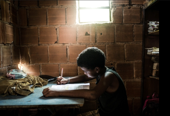 Menino pobre estudando com a luz que vem da janela da casa